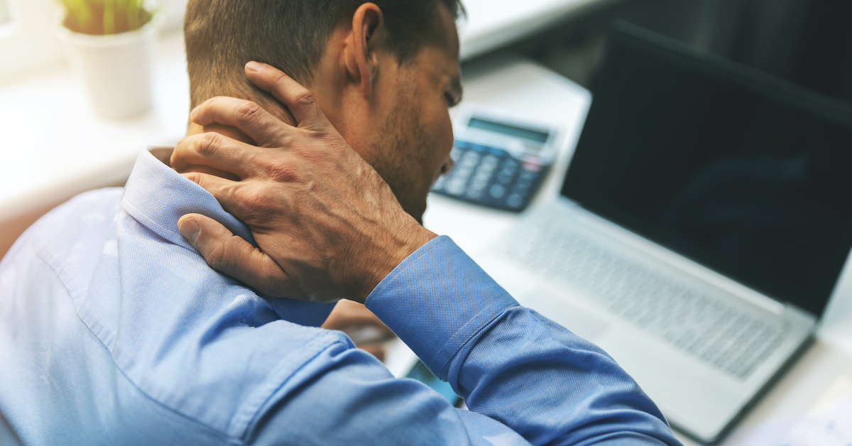 office syndrome - man suffering from neck and back pain while working with computer; blog: Neck Pain: Do You Need to See a Doctor?